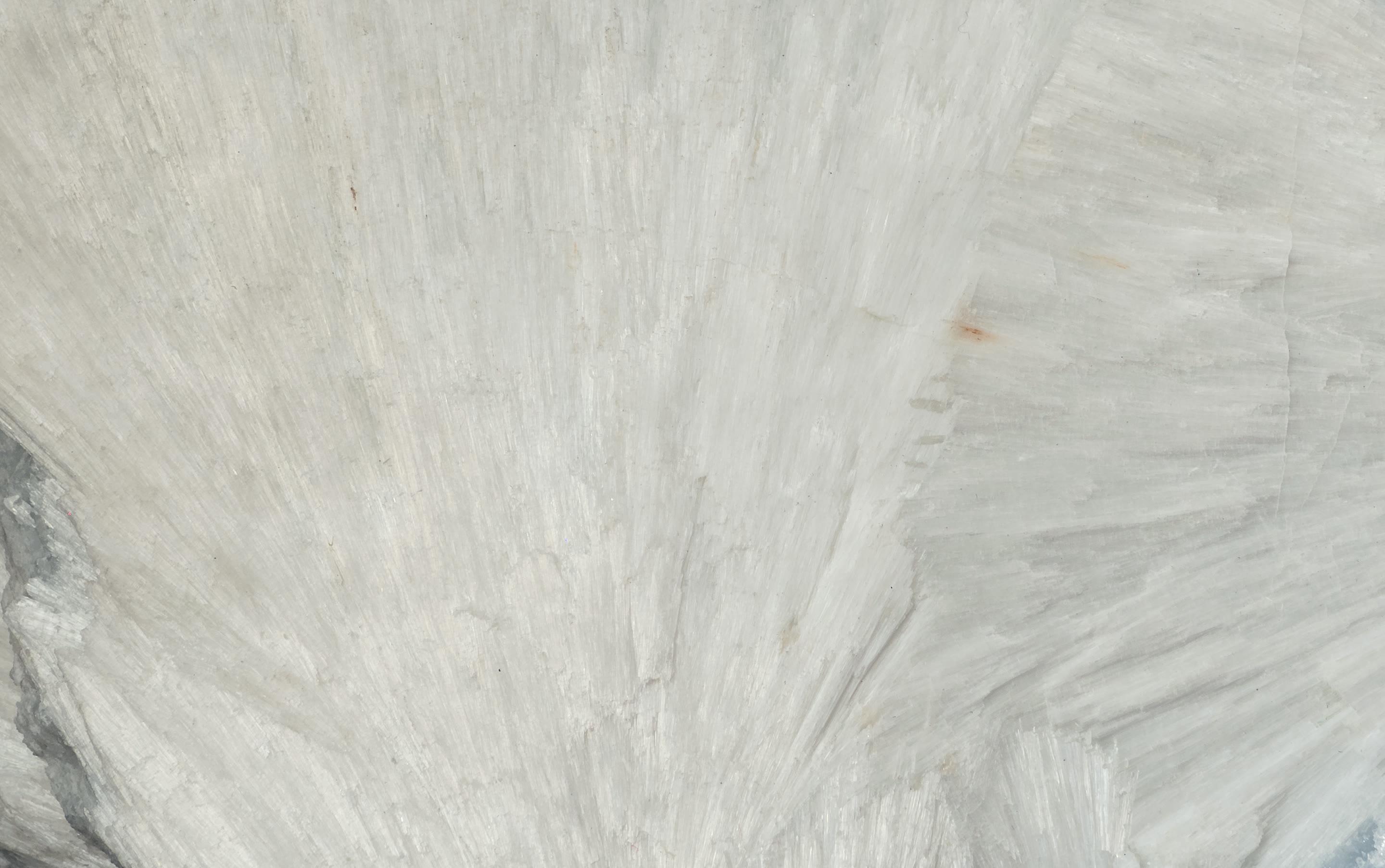 Close view of natural wollastonite: fans of fine white needle-shaped crystals radiating from a point